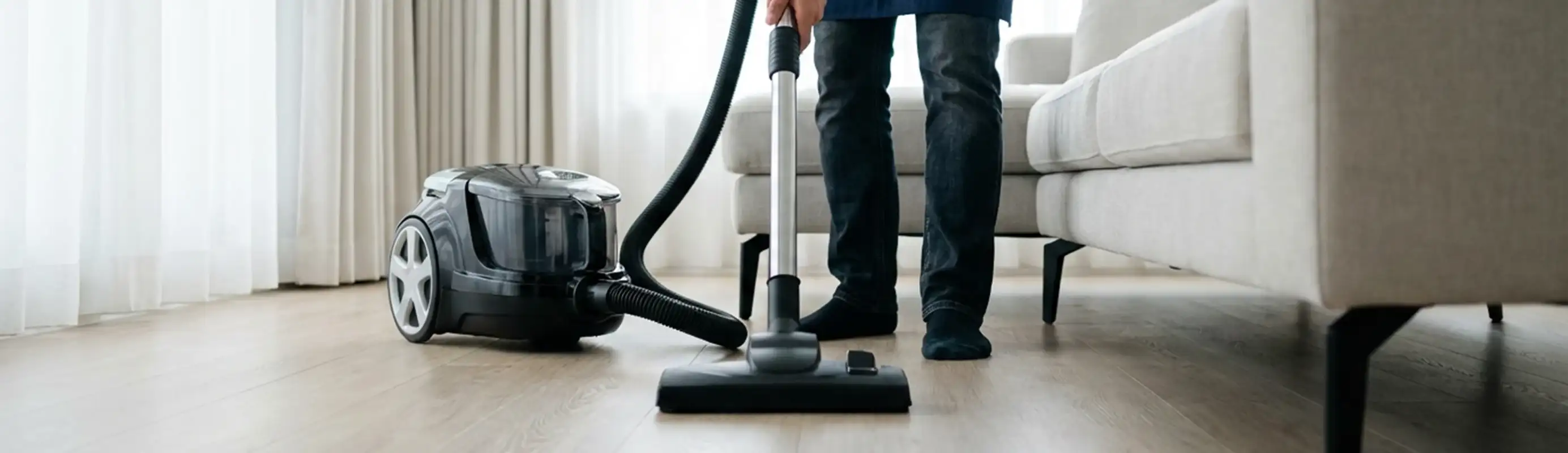 Professional house cleaner vacuuming a living room floor with a canister vacuum cleaner, San Diego, CA.