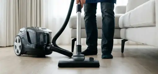 Professional house cleaner vacuuming a living room floor with a canister vacuum cleaner, San Diego, CA.