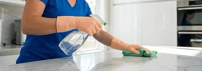 Maid service worker spraying and wiping a kitchen countertop with a microfiber cloth for sanitizing, San Diego, CA.