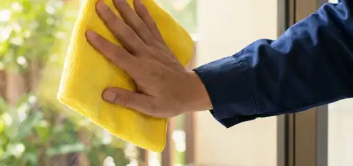 House cleaner wiping a glass window with a yellow microfiber cloth for streak-free cleaning, San Diego, CA.